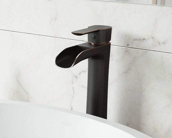 A warm antique-bronze vessel faucet on a stone basin, anchoring a vanity in a mixed-metal bathroom