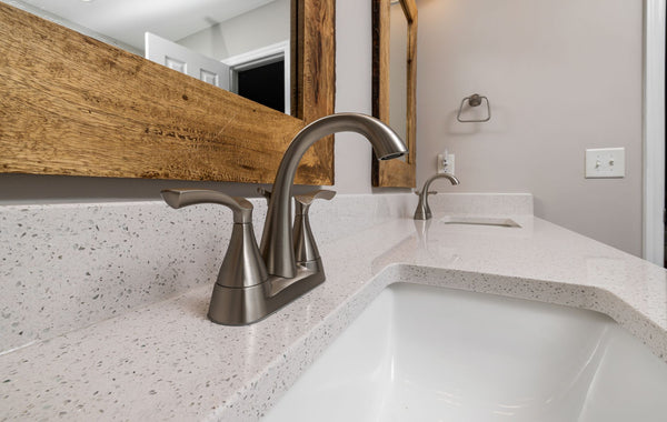 Close-up of a contemporary bathroom sink with a sleek faucet and wooden mirror frame
