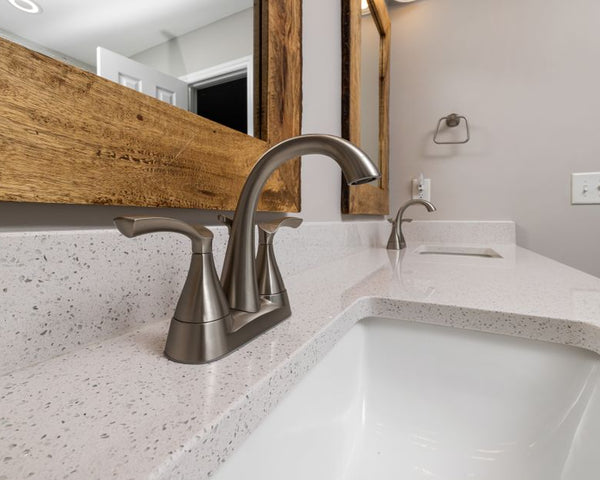 Close-up of a contemporary bathroom sink with a sleek faucet and wooden mirror frame
