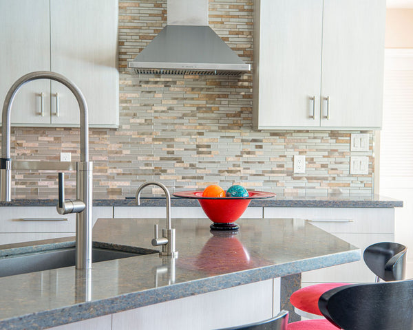 Contemporary kitchen interior with a sleek faucet and colorful fruit bowl on granite countertop.