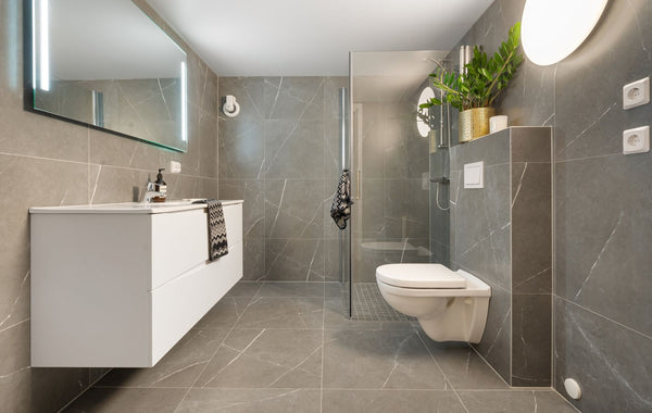 Stylish gray tiled bathroom featuring a shower, toilet, and illuminated mirror.