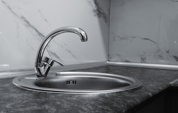 Stainless steel kitchen sink and faucet against marble backsplash in a modern kitchen.
