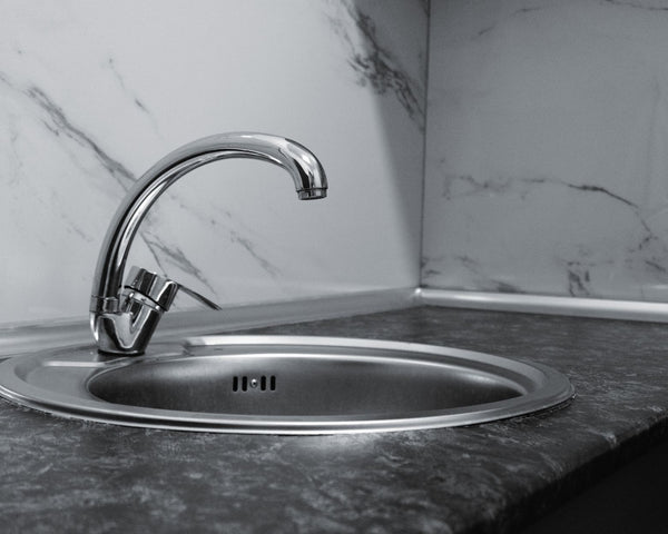 Stainless steel kitchen sink and faucet against marble backsplash in a modern kitchen.