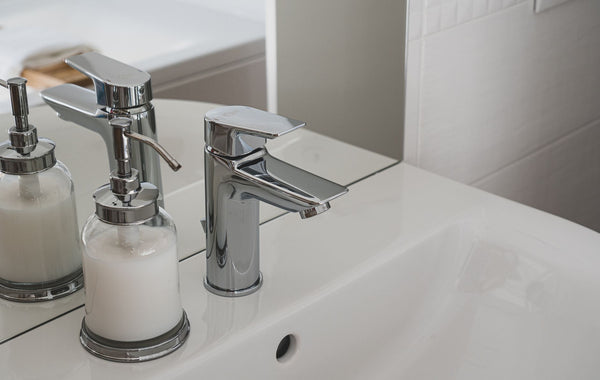 A sleek chrome faucet and soap dispenser on a pristine white sink in a modern bathroom setting.