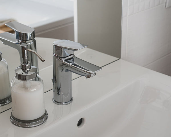 A sleek chrome faucet and soap dispenser on a pristine white sink in a modern bathroom setting.