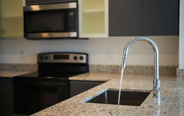 A sleek kitchen faucet on a granite countertop with modern appliances in view.
