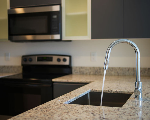 A sleek kitchen faucet on a granite countertop with modern appliances in view.