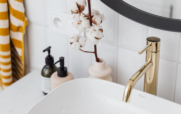 A stylish bathroom with a gold faucet, cotton plant, and modern accessories.