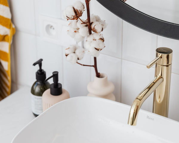 A stylish bathroom with a gold faucet, cotton plant, and modern accessories.