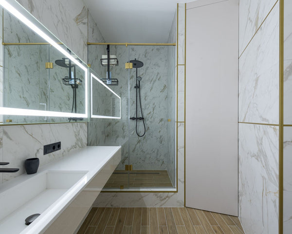 Shower cabin and ceramic sink in spacious modern bathroom with marble tiled walls and big window with bright lamps