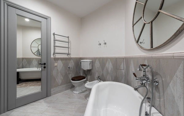 White bathtub with faucet at tiled wall placed near toilet and bidet in contemporary bathroom with mirror with reflection on door