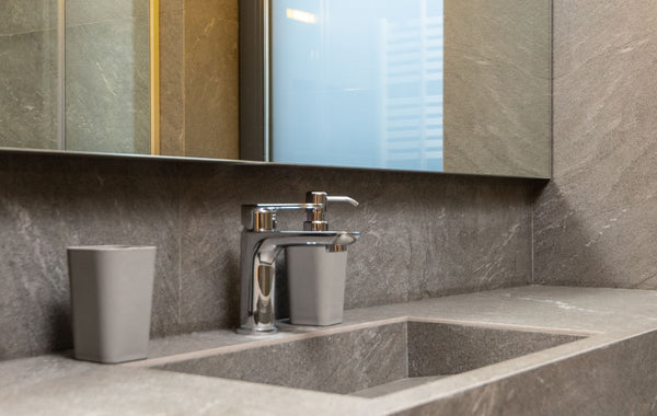 Chrome faucet and marble sink under mirror in modern bathroom with tiled walls