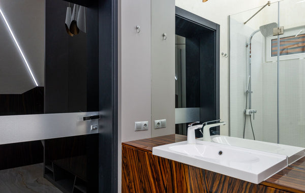 White ceramic sink with chrome faucet on wooden cabinet and shower cabin with glass walls in modern bathroom