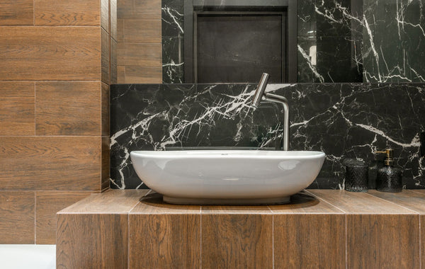 White sink and faucet in stylish modern bathroom with marble and wood look tiles