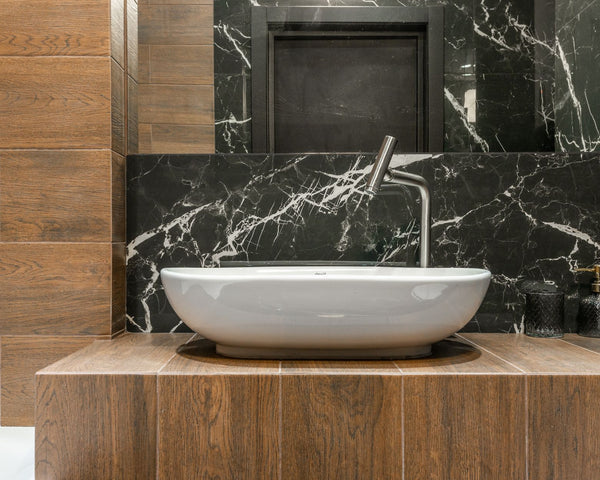 White sink and faucet in stylish modern bathroom with marble and wood look tiles