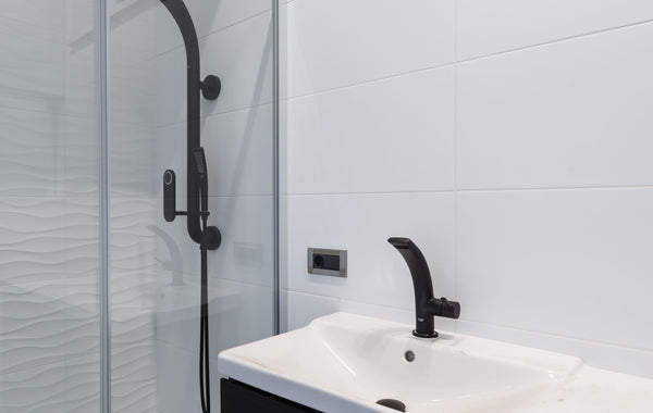 Modern minimalist style interior design of bathroom with white tiled walls and washbasin and black faucet and shower unit with glass partition