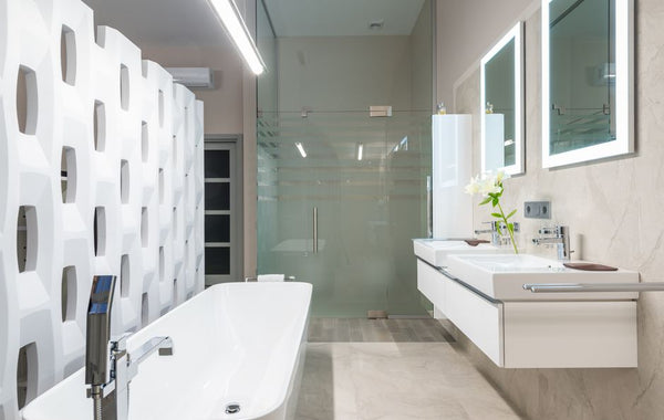 White bathtub with tap near decorative partition placed near sink and mirrors in stylish light bathroom with glass shower cabin