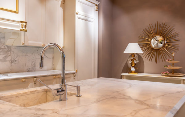 Sink with faucet on marble counter in modern stylish kitchen with white cabinets and glowing lamp near decorations in apartment