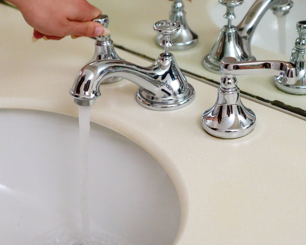 Hand operating a chrome faucet with running water in an elegant bathroom setting.
