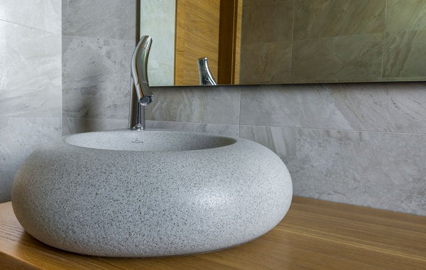 Elegant stone bathroom sink with modern chrome faucet and large mirror.
