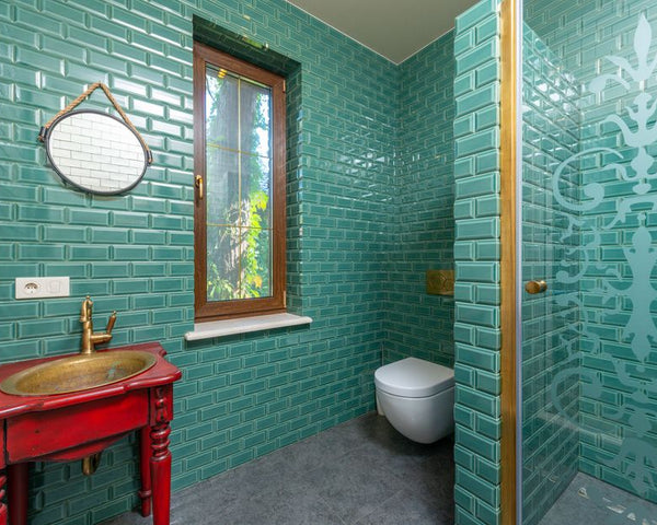 Modern bathroom with green tiled walls, gold fixtures, and elegant decor.